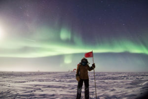 Blaise Kuo Tiong stands in the snow, holding a flag, in Antarctica.